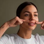 Middle-aged woman looking in the mirror and touching smile lines around her mouth before Botox or filler treatment.