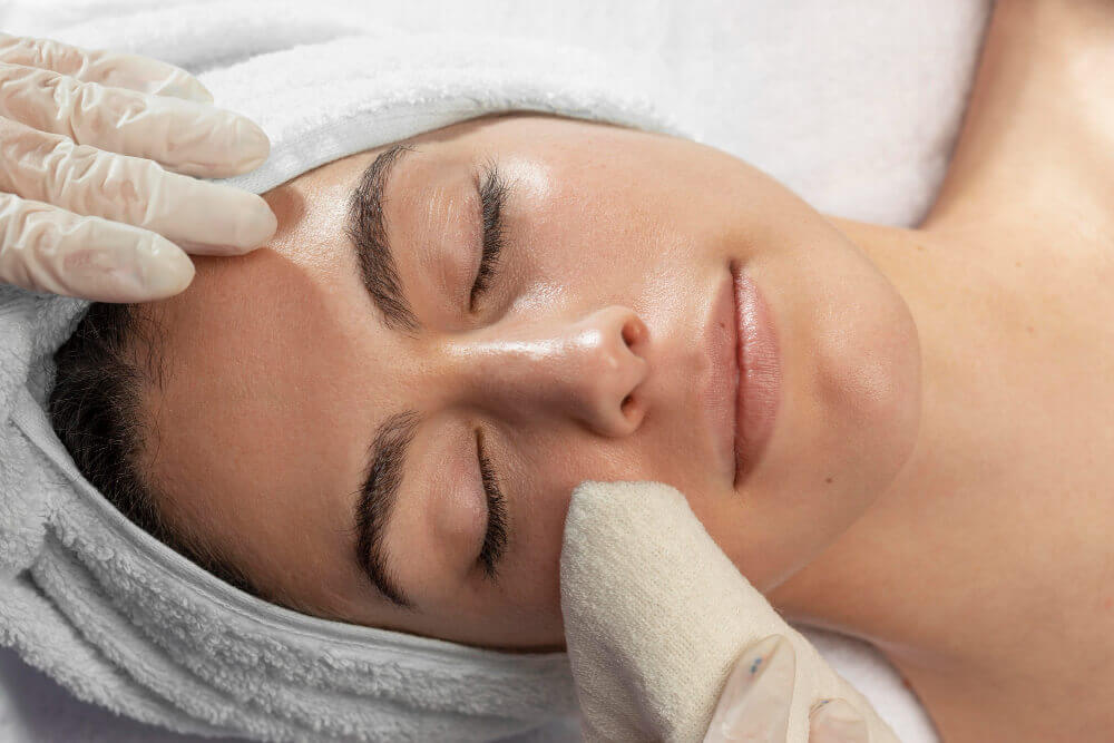 Client having facial skin cleansed before dermaplaning exfoliation treatment